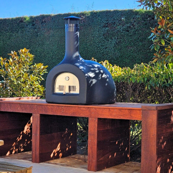 outdoor pizza oven on a wooden table with greenery 