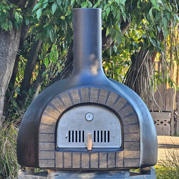 Outdoor brick oven with a chimney against a green leafy background