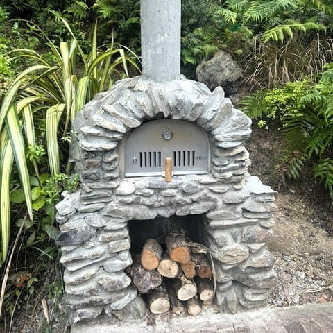 Stone-built outdoor oven with wood inside, surrounded by greenery