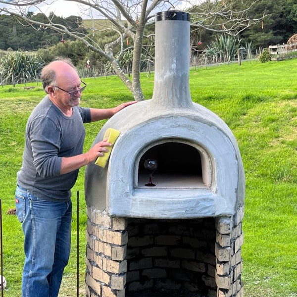 Man cleaning an outdoor stone oven in a grassy area