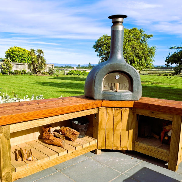 Outdoor pizza oven on a wooden platform with a garden view