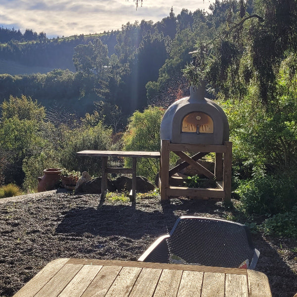 Outdoor setting with a wooden table, chairs, and a pizza oven