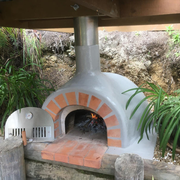 Outdoor brick oven with fire inside, surrounded by greenery