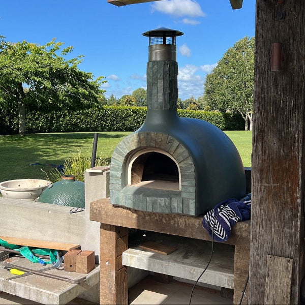 Outdoor pizza oven in a garden setting with greenery