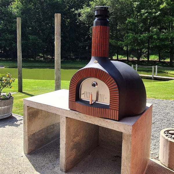 Wood-fired pizza oven on a stand outdoors with greenery