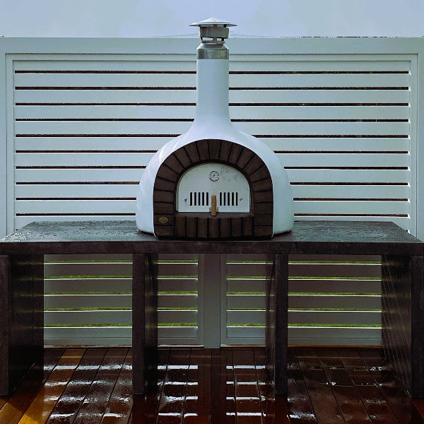 White outdoor pizza oven on a wooden stand with a white slatted background