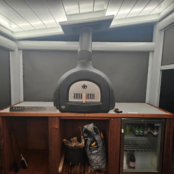 Gray pizza oven on a wooden stand with a refrigerator underneath,