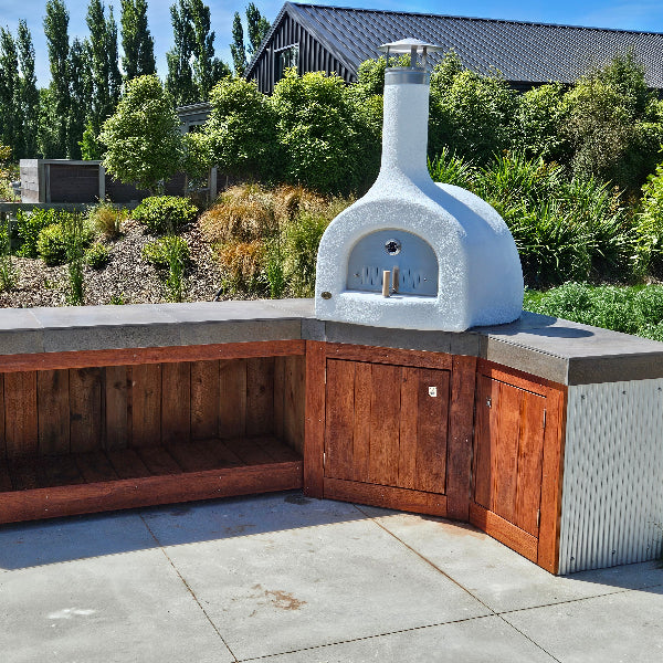 Outdoor pizza oven integrated into a wooden outdoor kitchen setup with a garden background.