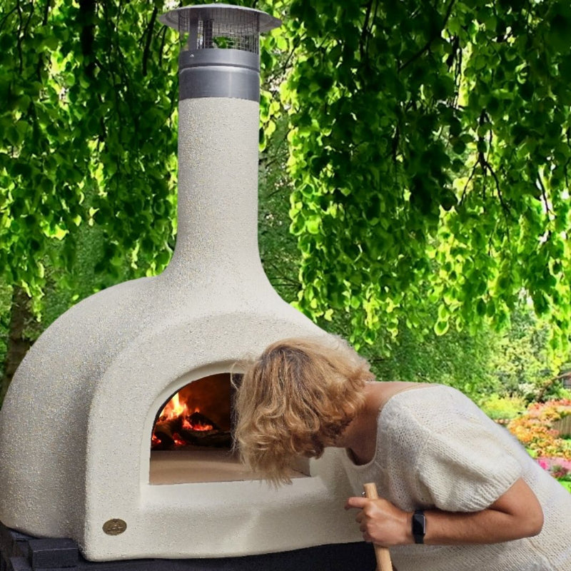 Person using an outdoor pizza oven with a green garden background
