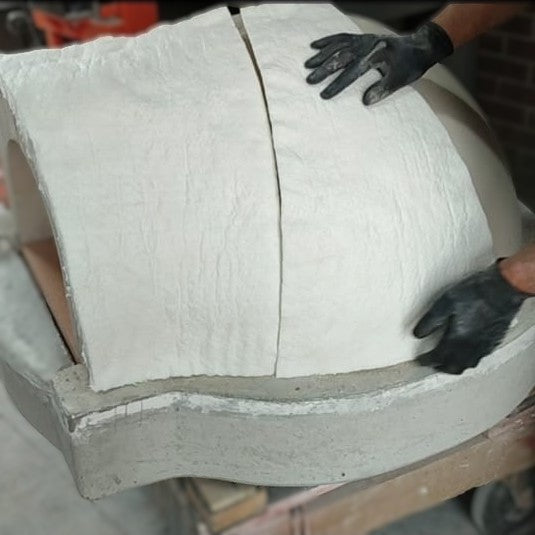 Ceramic fibre blanket being installed over the refractory dome of a wood-fired pizza oven.
